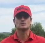 rostro de golfista mirando a cámara. Lleva gorra y camiseta rojas. Se ven parcialmente sus hombros. Al fondo, arboleda y cielo.